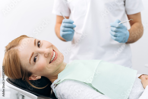 Charming woman sitting in a dental chair, looking at the camera. The dentist examines the teeth with the help of dental instruments