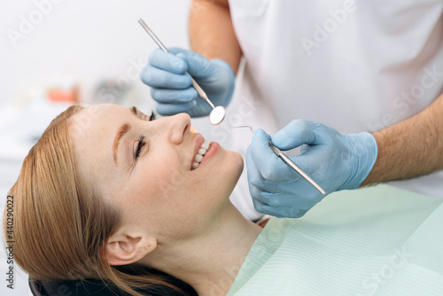Attractive, charming woman sitting in a dental chair. The dentist examines the teeth with the help of dental instruments