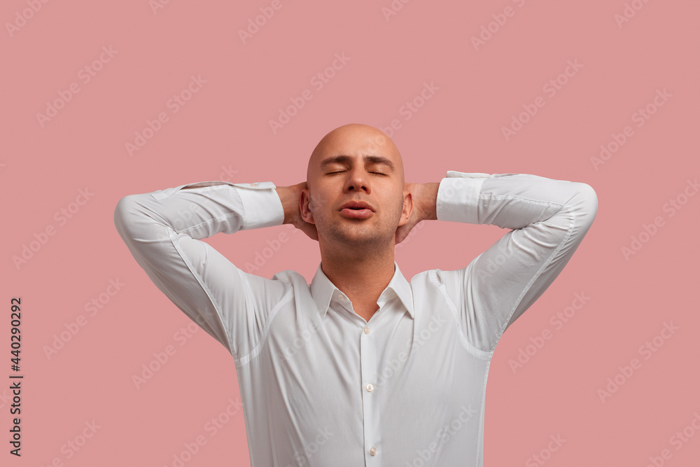 I can relax everywhere. Horizontal photo shot of relaxed carefree bald guy in white shirt, keeps hands behind head, has calm expression, isolated over pink background. I can relax everywhere. Horizontal photo shot of relaxed carefree bald guy in white shirt, keeps hands behind head, has calm expression, isolated over pink background.