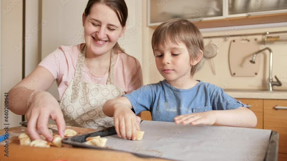 Smiling boy with mother making biscuits and putting them on baking sheet. Children cooking with parents, little chef, family having time together, domestic kitchen. Smiling boy with mother making biscuits and putting them on baking sheet. Children cooking with parents, little chef, family having time together, domestic kitchen.
