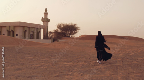 Portrait of a young Arab woman wearing traditional black clothing during beautiful sunset over the desert. photo