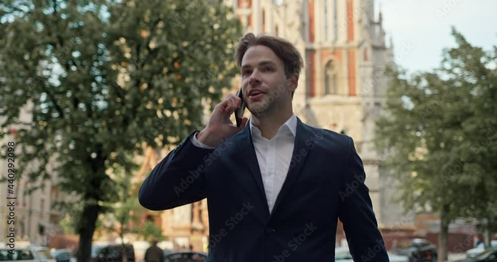 Busy Handsome Businessman hurries to Meeting checking time on Wristwatch. Talking using Smartphone while walking down the street. Wears Luxury suit. Attractive Business Person. Young Entrepreneur. Busy Handsome Businessman hurries to Meeting checking time on Wristwatch. Talking using Smartphone while walking down the street. Wears Luxury suit. Attractive Business Person. Young Entrepreneur.
