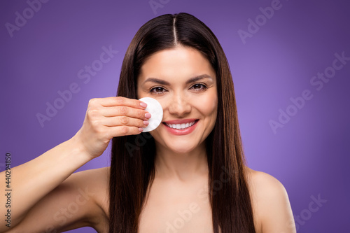 Photo of cute charming mature woman naked shoulders smiling removing make up cotton pad isolated violet color background