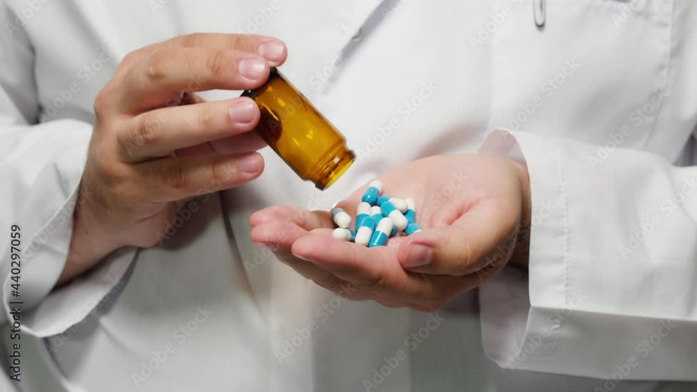 Doctor putting medicine tablets into hand wearing medical gown, shooting of pouring out blue and white drugs in palm from brown bottle. A lot of pills, the concept of the pharmaceutical industry. Doctor putting medicine tablets into hand wearing medical gown, shooting of pouring out blue and white drugs in palm from brown bottle. A lot of pills, the concept of the pharmaceutical industry.