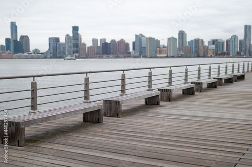 Row of Empty Wood Benches on a Pier along the Hudson River with the Jersey City Skyline in the Background in New York City