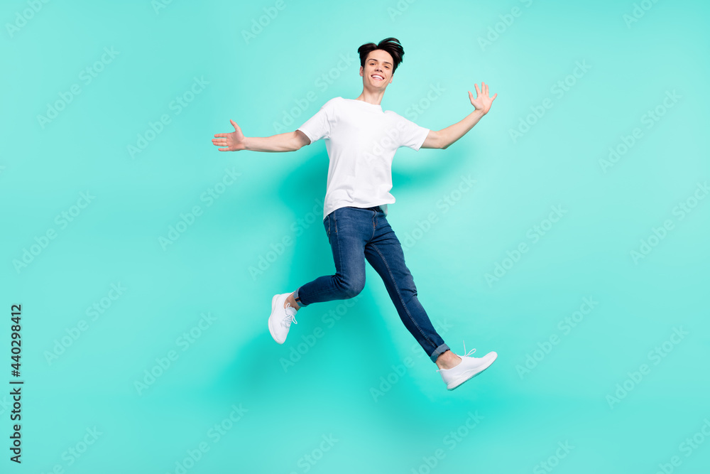 Full body profile photo of cool brunet hairdo teenager guy jump wear t-shirt jeans isolated on teal background