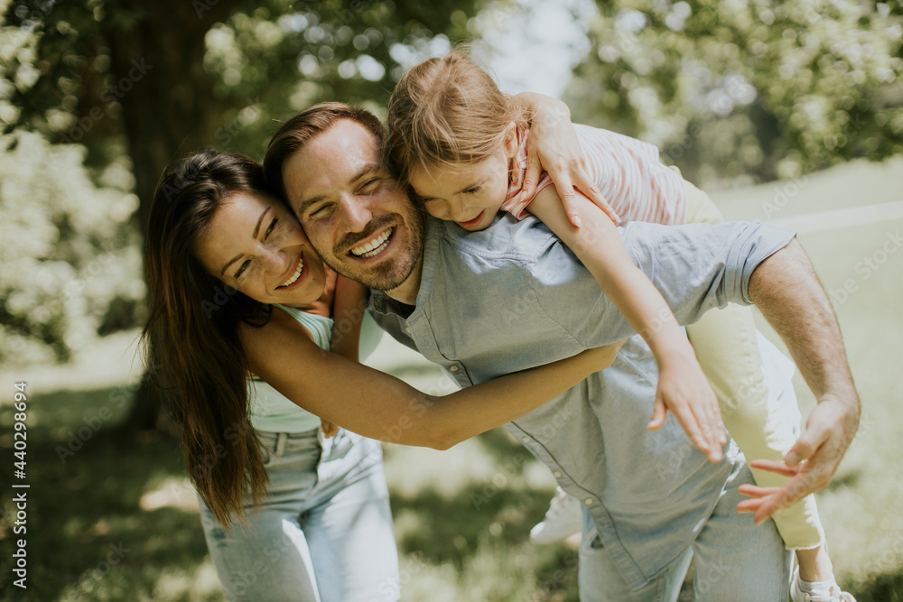 Fototapeta premium Happy young family with cute little daughter having fun in the park on a sunny day