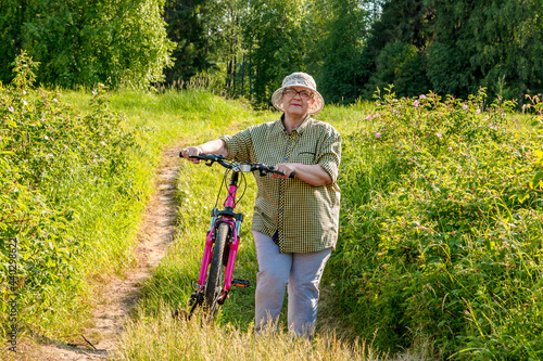 Elderly woman with a bike on the path. Grandma rides a bike.