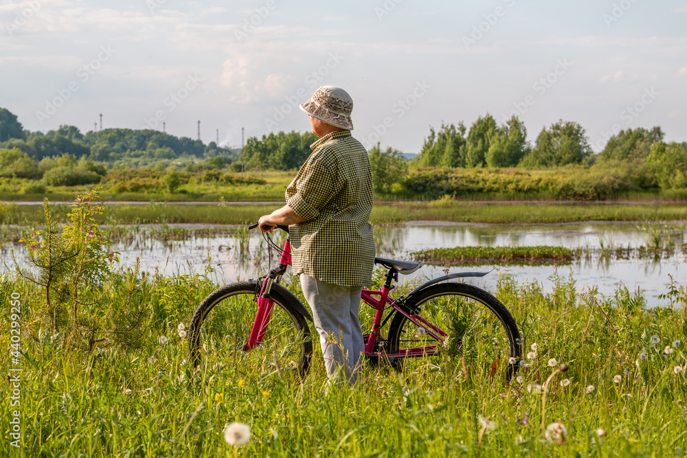 Obraz premium Grandmother with a bike by the lake. An elderly woman rides a bicycle.