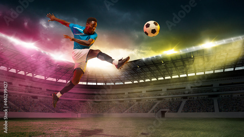 Goal. Male african socce, football player jumping in attack during sport match on cloudt sky background at stadium photo