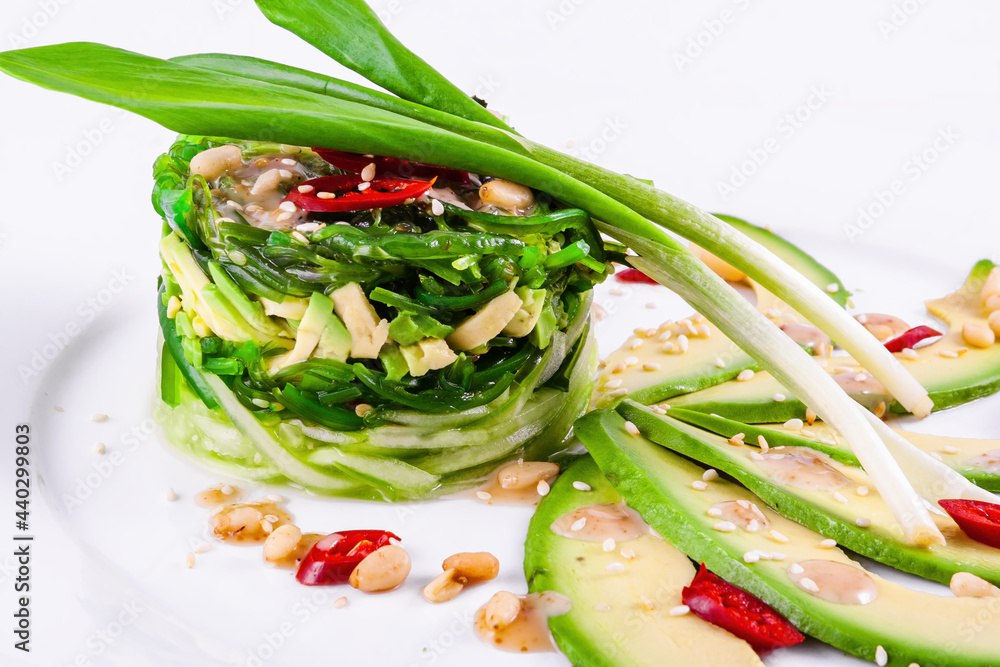 Salad with chuka seaweed, avocado, cucumber, sesame seeds, pine nuts on a white plate
