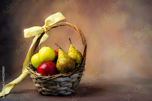 Scena con un cesto di frutta pieno di mele e pere rosse e gialle, legato con un fiocco giallo. Con spazio per scrivere. Alimentazione. Salute. Ringraziamento.