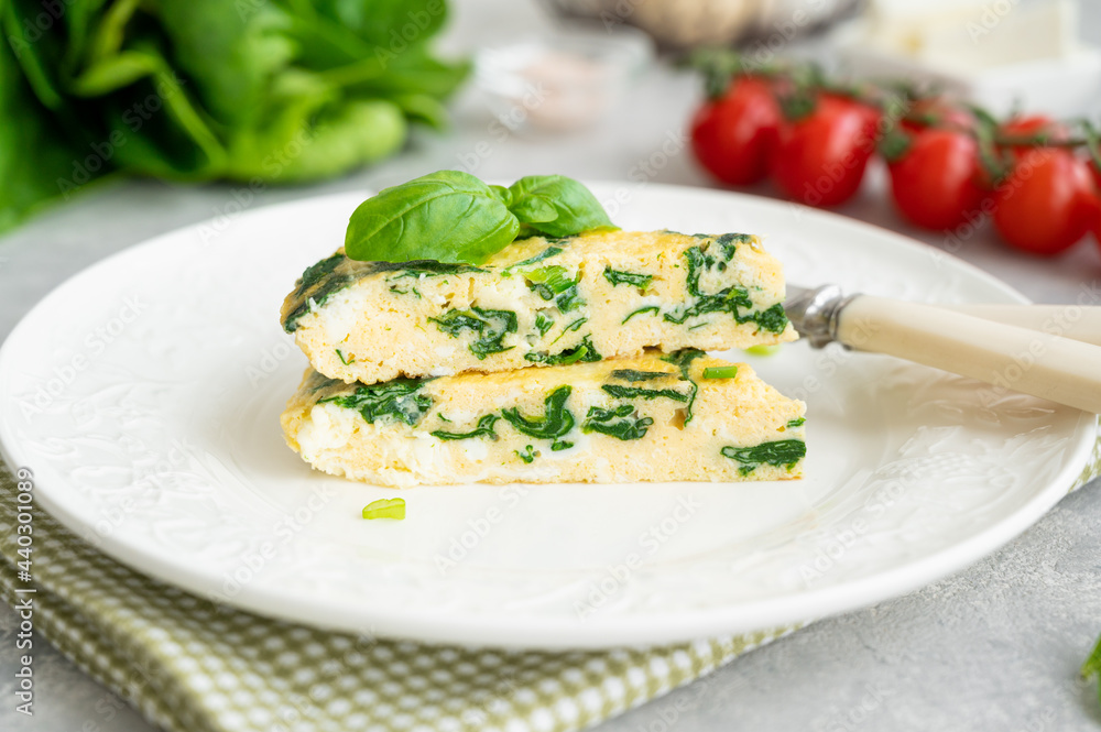 Omelette with spinach, green onions and feta cheese on a white plate on a gray concrete background. Healthy breakfast. Copy space. Omelette with spinach, green onions and feta cheese on a white plate on a gray concrete background. Healthy breakfast. Copy space.