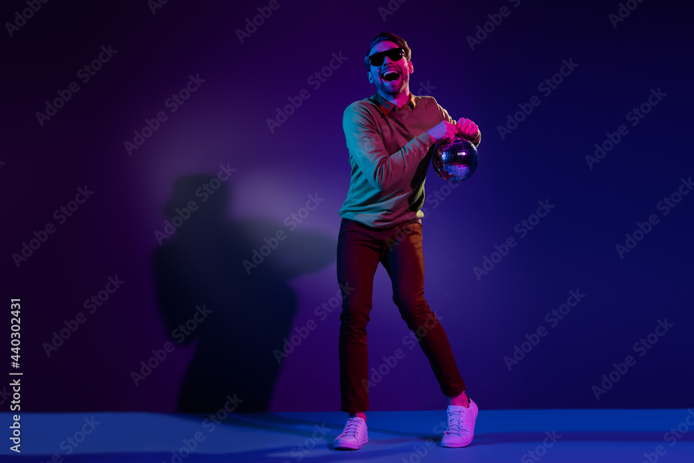 Full length photo of funny young positive man dance good mood hold disco ball isolated on neon background