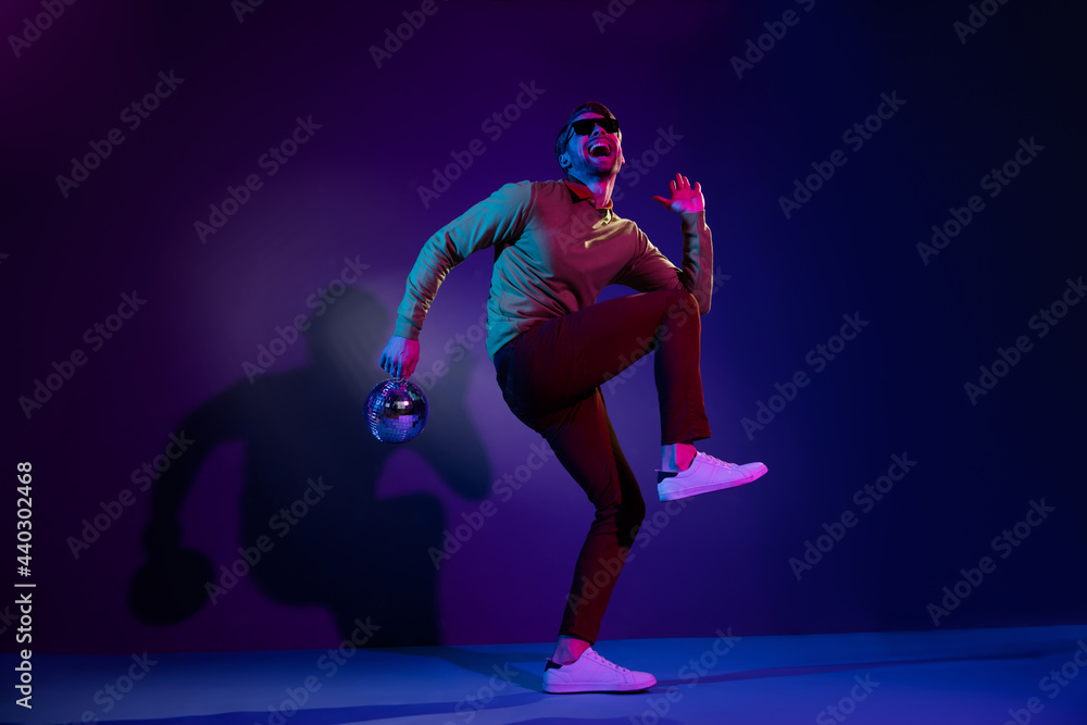 Full length body size photo man in sunglass dancing on discotheque keeping disco ball isolated on violet color background