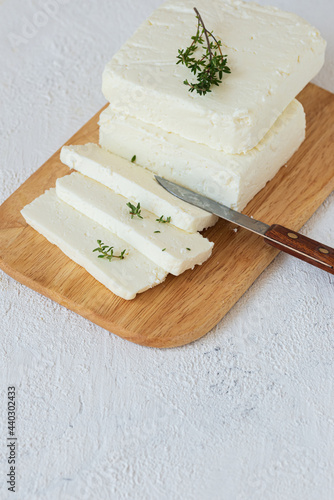 Paneer, tofu,  soy cheese,  or brynza, feta with thyme and a knife on a wooden cutting board on a light background photo