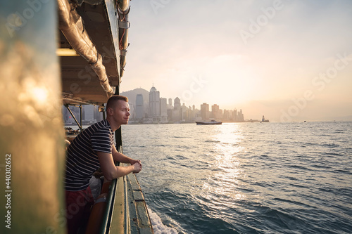 Pensive man looking from ferry boat against urban skyline st beautiful sunset. Tourist in Hong Kong. photo