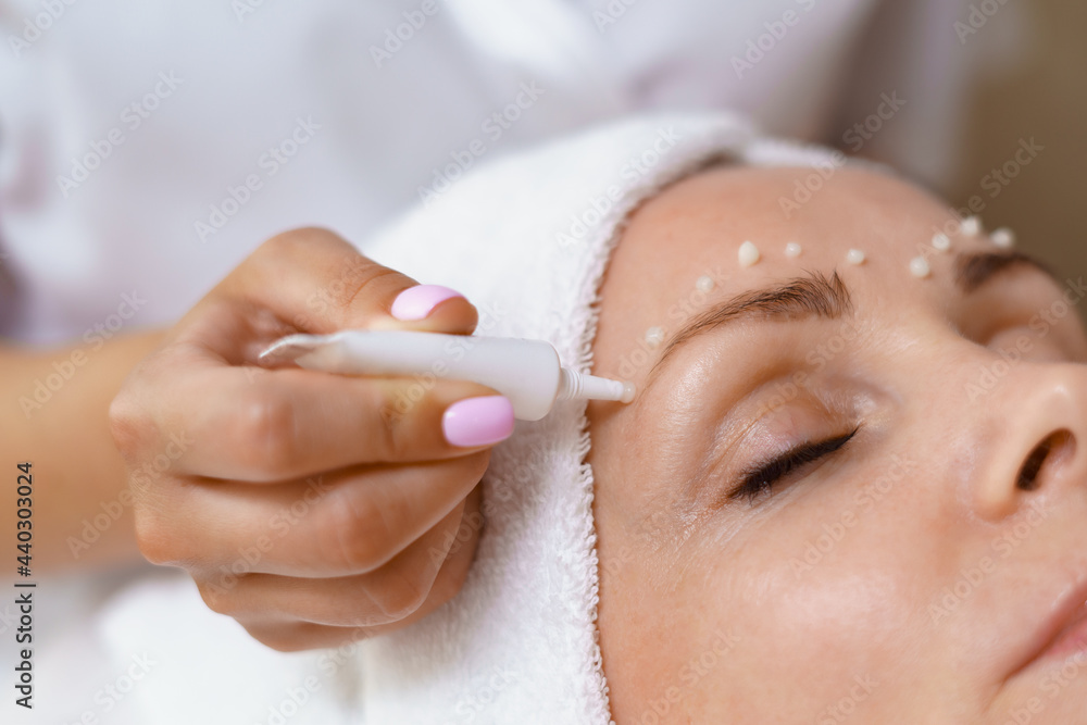 Face and Eye cream treatment or therapy. Dermatologist applying lotion on female skin