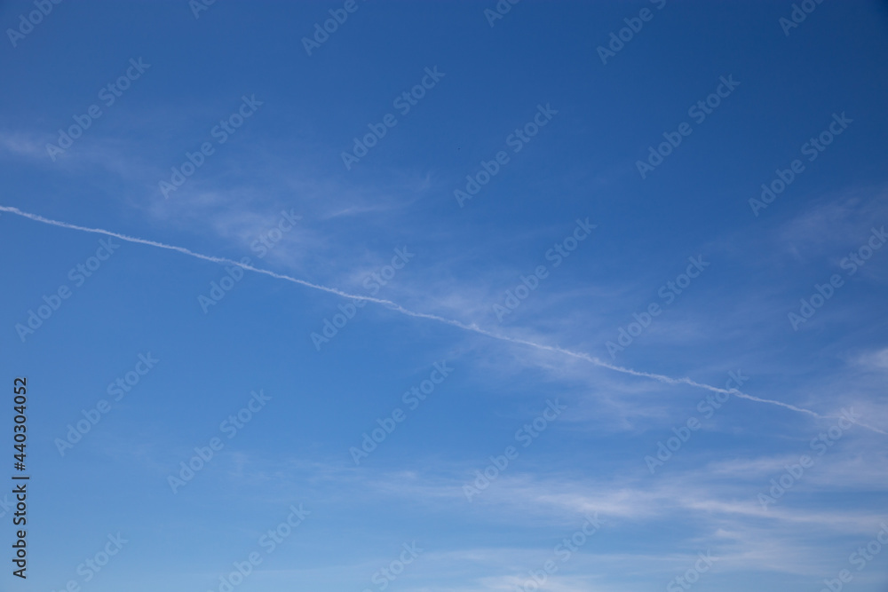 Wide blue sky with few thin clouds and typical airplane trail cutting across the sky Wide blue sky with few thin clouds and typical airplane trail cutting across the sky