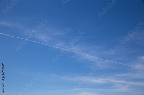 Wide blue sky with few thin clouds and typical airplane trail cutting across the sky