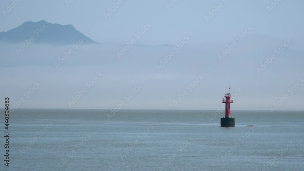 Red navigational buoy floating in Yellow sea between islands, a mountain covered in haze near Ganghwado island, South Korea Red navigational buoy floating in Yellow sea between islands, a mountain covered in haze near Ganghwado island, South Korea