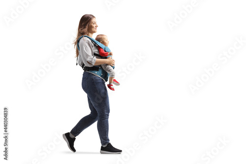 Full length profile shot of a mother walking and carrying a baby in a carrier