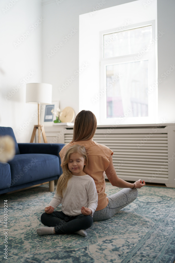 Young mother with little daughter practicing yoga at home. Family fizical activity, sporty mom and kid Young mother with little daughter practicing yoga at home. Family fizical activity, sporty mom and kid