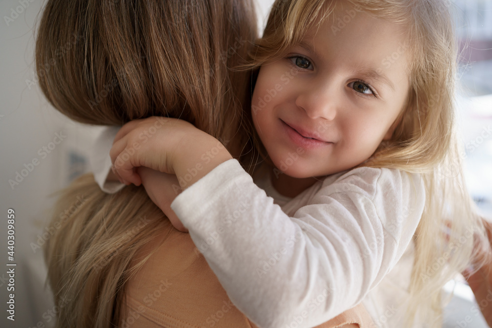 Beautiful young woman and her charming little daughter are hugging and smiling at home Beautiful young woman and her charming little daughter are hugging and smiling at home