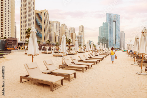 Photography Woman tourist walks barefoot in the sand between rows of sun loungers and beach umbrellas in the JBR district in Dubai