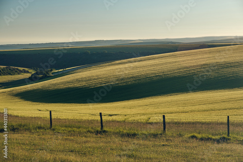 Farmland on a sunny evening in the South Downs National Park with the sun setting over the Sussex Weald. A simple fence in the foreground. 