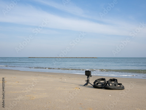 action camera lay beside the sandle on the sand beach with blue sky background