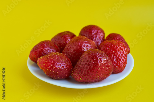Big red strawberries on white plate on yellow background close up