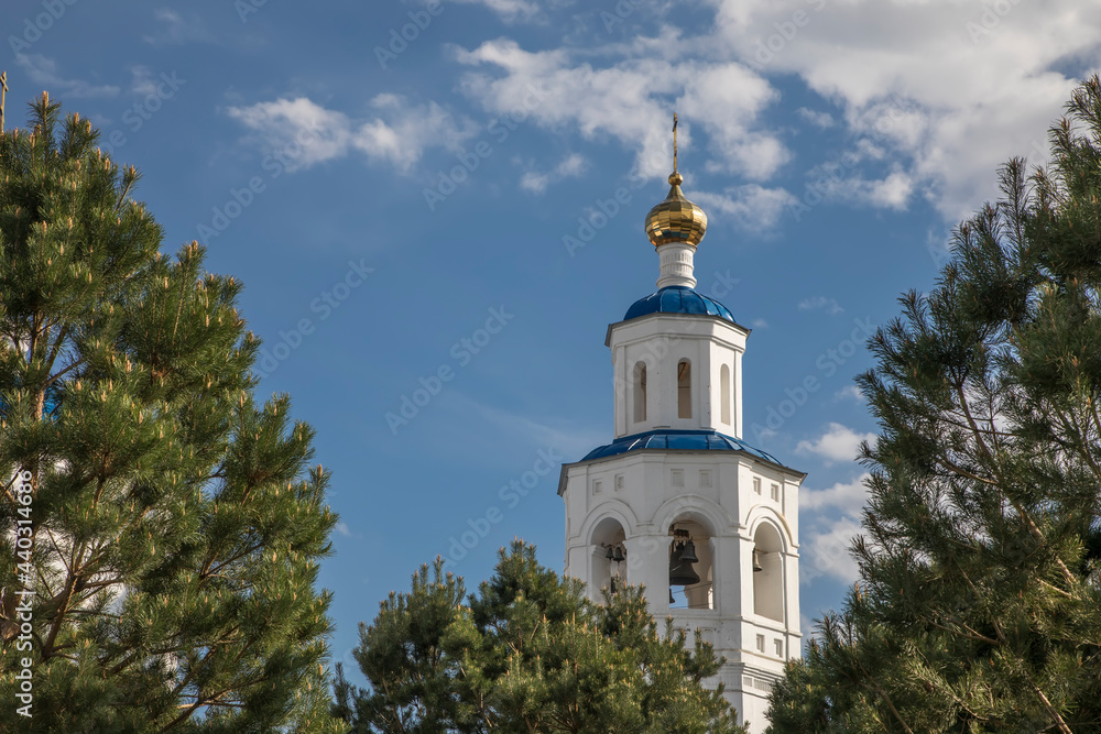 A beautiful white tower with a dome among the trees. An old church. Sunny day. Harmony with nature