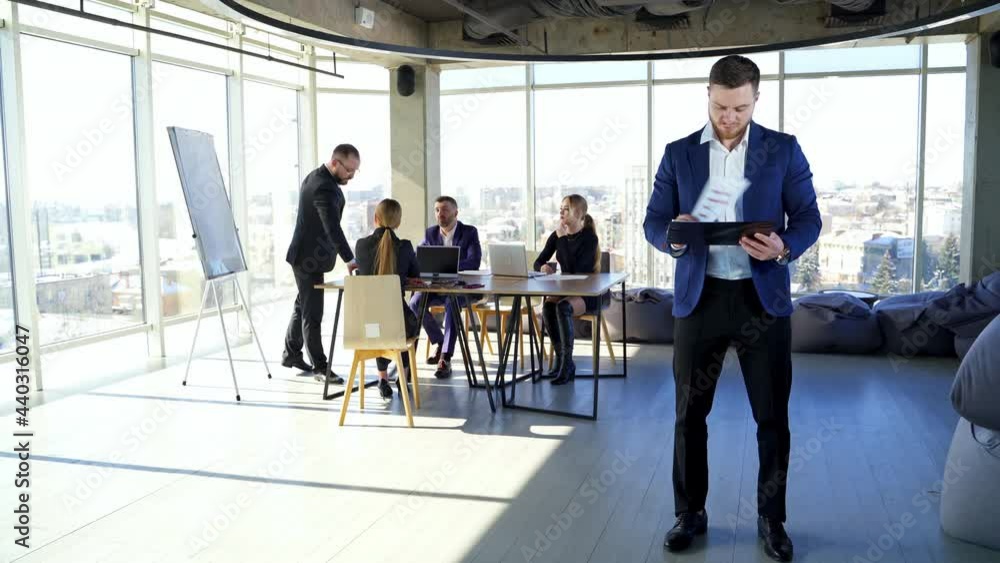 Handsome businessman looking into tablet in background of meeting. Business meeting. Handsome businessman looking into tablet in background of meeting. Business meeting.