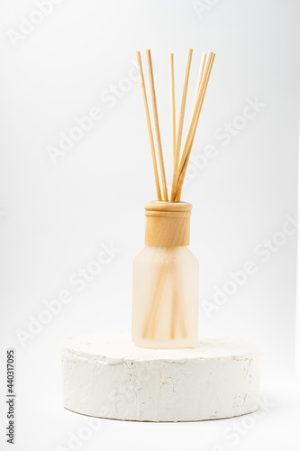 Aroma bottle glass and wooden sticks staying on cement white podium on white background