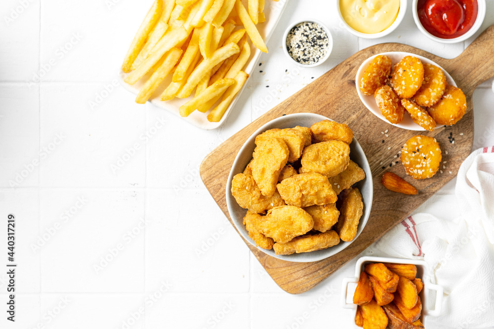Chicken nuggets, strips, french fries, fried potatoes, ketchup and cheese sauce on a light background. Fast food top view