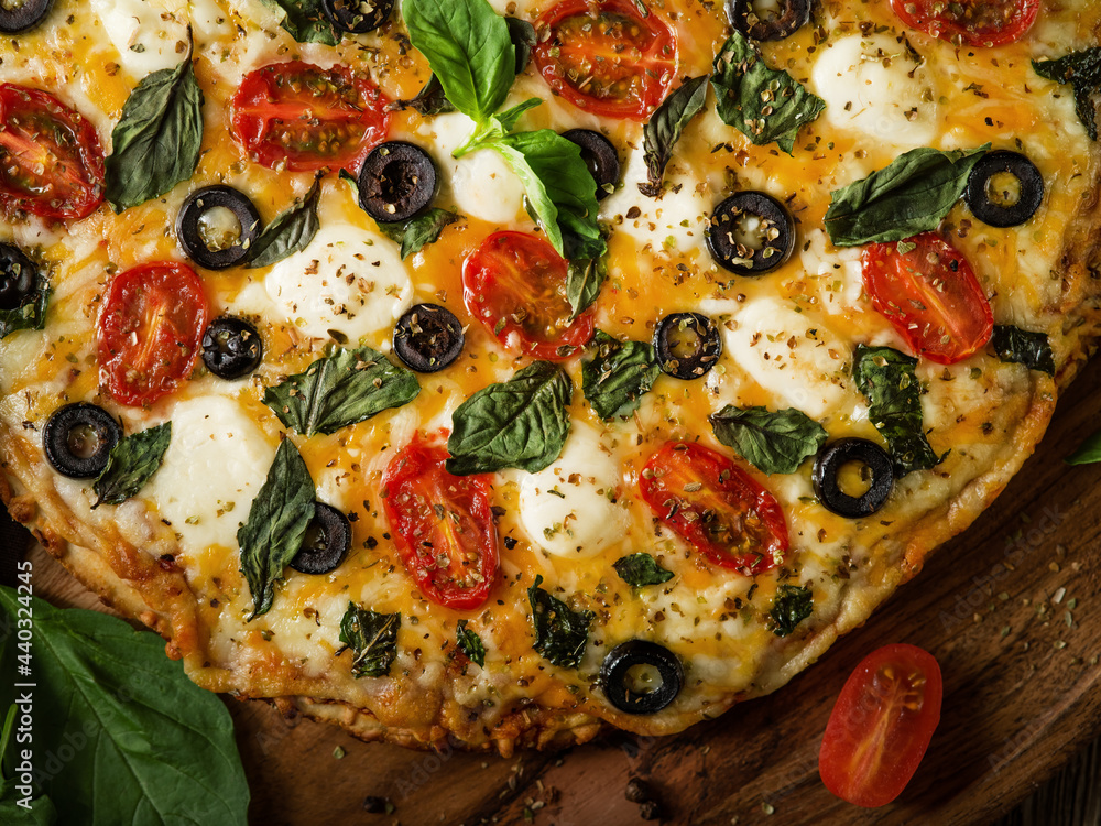 In the photo we see pizza. Close-up. High angle view. Careful viewing. Macro photography. Near the pizza, on a wooden table, there is a small tomato and a leaf of green mint.