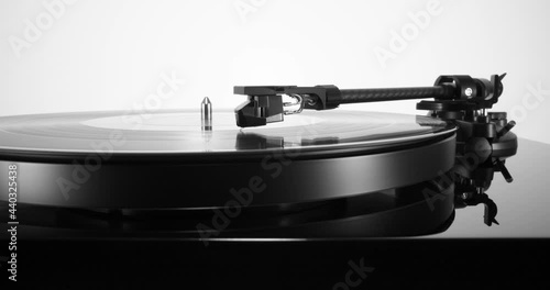 Pull-out with black turntable with spinning vinyl record on. White background, macro view of tonearm headshell photo