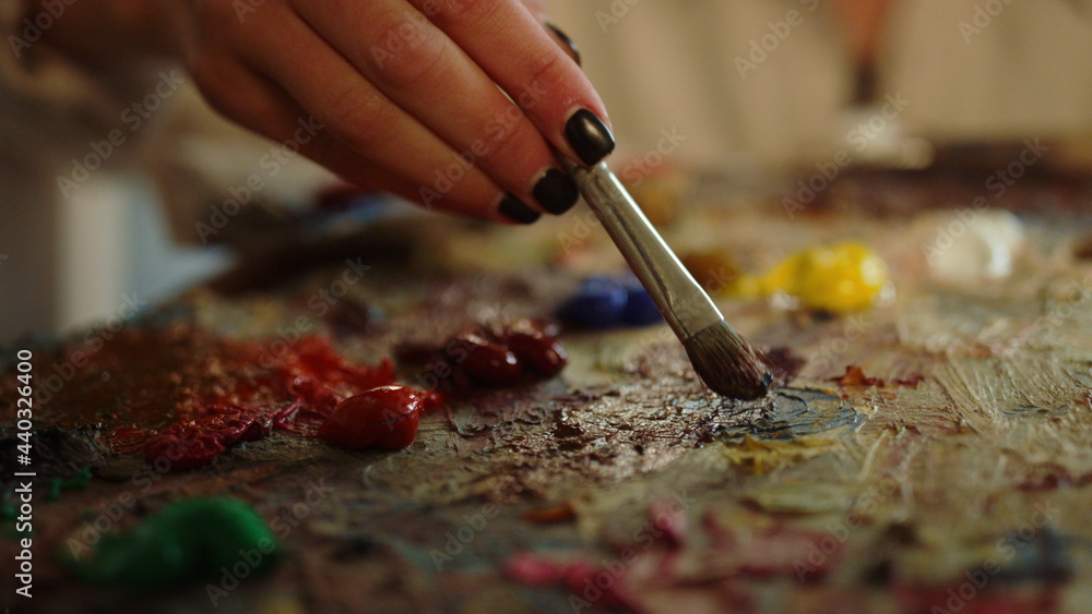 Unrecognizable woman taking paints on palette. Artist having brush in hand.