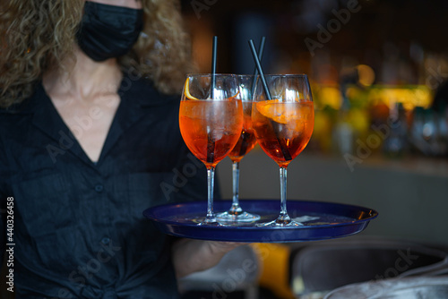 masked waitress carries cocktails on a tray