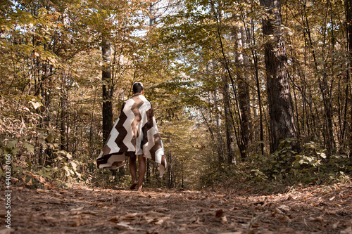 A young and handsome guy walks in the morning through the woods wrapped in a blanket. The body of a man in a blanket.