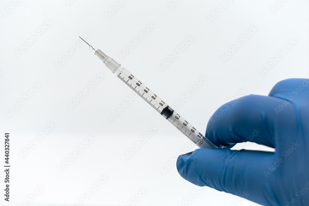 Medical syringe with a needle at the end of the drop. Hand with blue medical glove. White background. Medical syringe with a needle at the end of the drop. Hand with blue medical glove. White background.