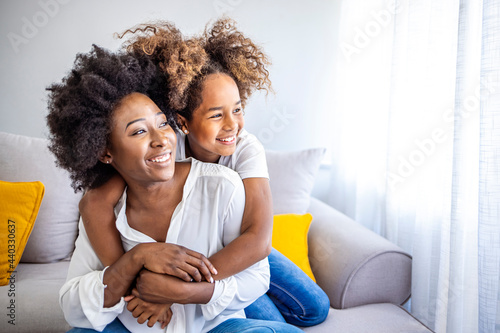 Shot of an adorable little girl and her mother in a warm embrace at home. Loving young mother laughing embracing smiling cute funny kid girl. Head shot close up happy young mother bonding 