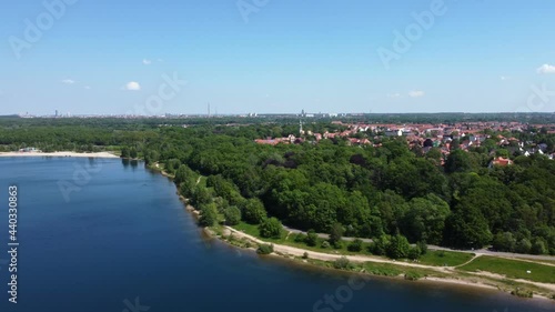 Drone flight with panoramic view of a lake and surrounding forest. In the background: the skylines of the cities of Markkleeberg and Leipzig (German: Cospudener See)
