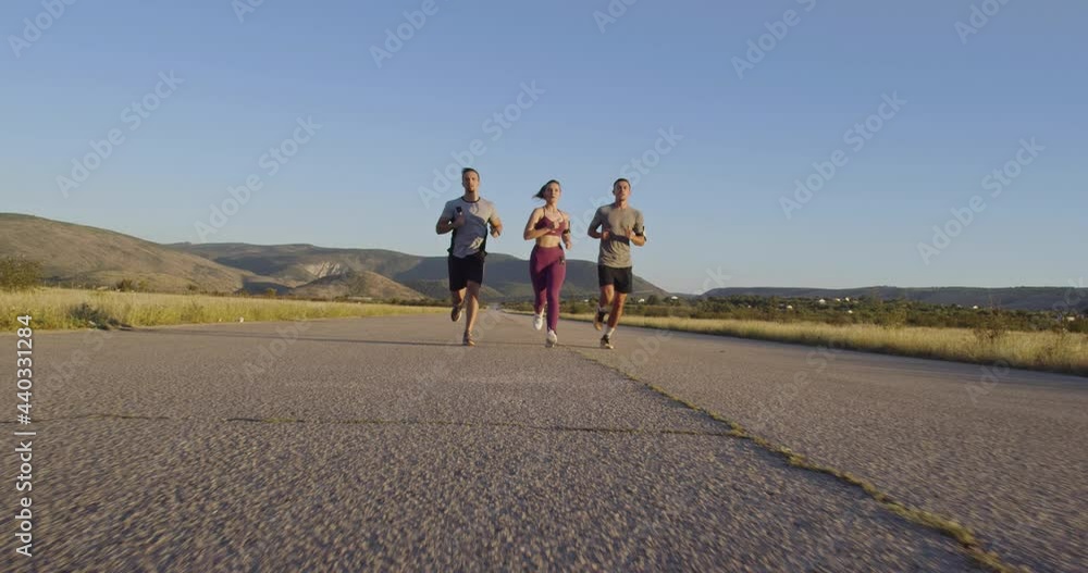 Multiethnic group of athletes running together on a panoramic countryside road. Diverse Team of joggers on morning training. Multiethnic group of athletes running together on a panoramic countryside road. Diverse Team of joggers on morning training.
