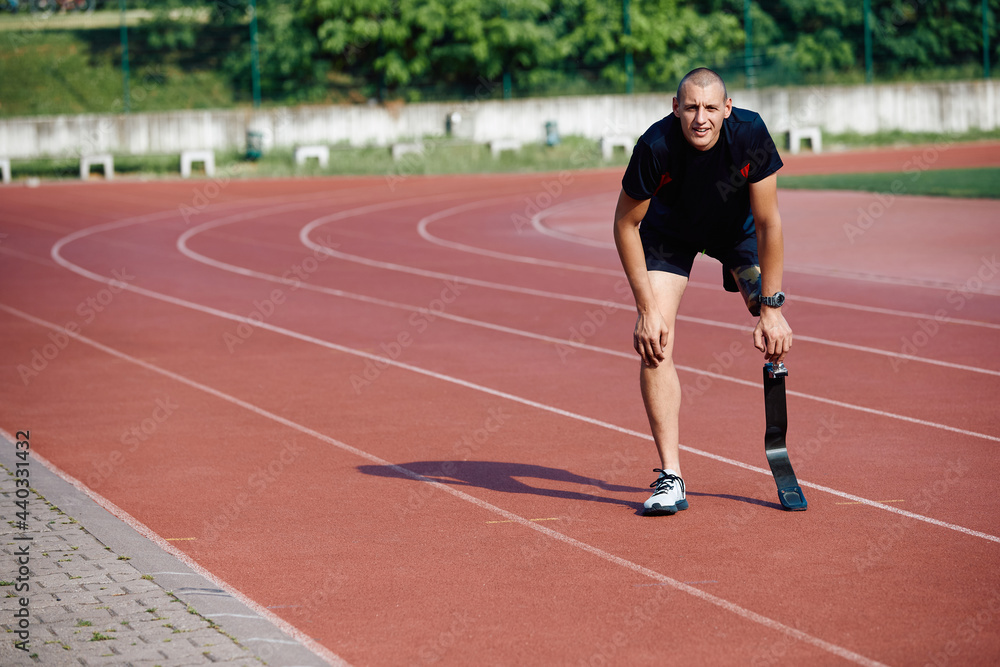 Male runner with prosthetic leg taking a break and rests at running track during sports training at the stadium.