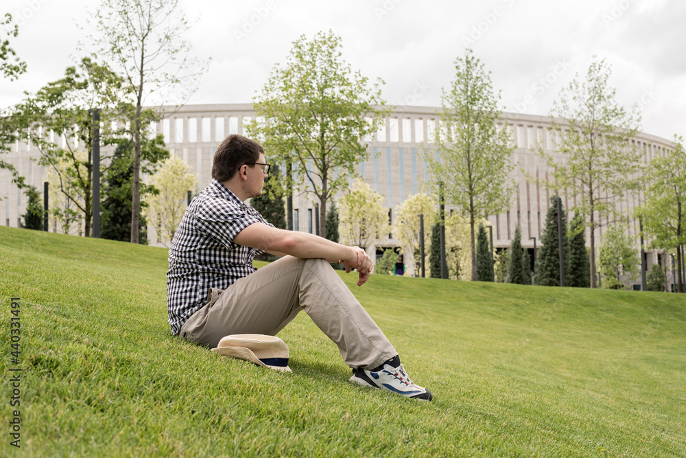Young thoughtful man sitting on the grass in the park Young thoughtful man sitting on the grass in the park