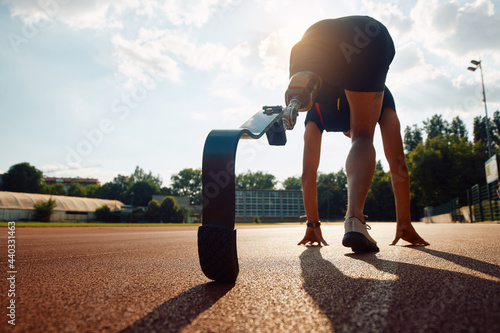 Rear view of runner with prosthetic leg at starting line on running track at the stadium.