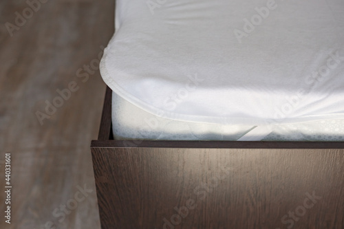 Wooden bed with a high mattress and a covered white mattress cover