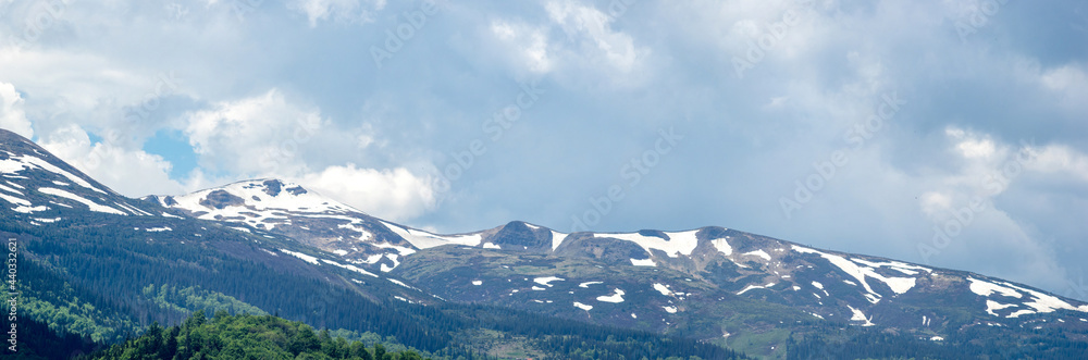 Spring mountains in the snow on the background of a green forest
